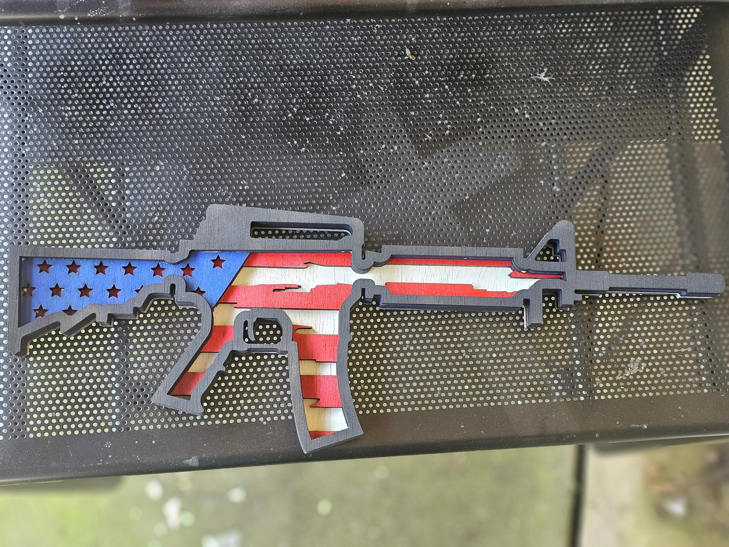 Custom wooden rifle sign with American flag design by Bearnugget Customs, displayed on metal mesh.
