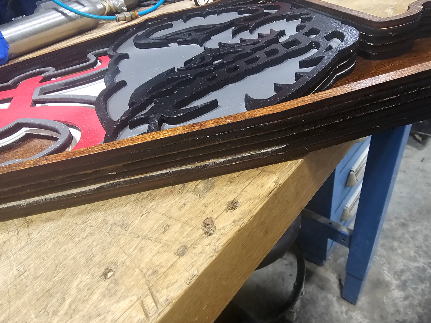 Custom layered wood sports sign with intricate painted design on workbench at BearNugget Customs