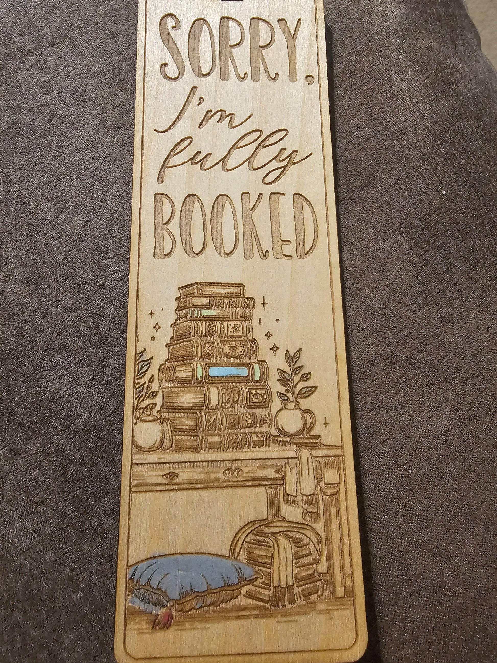 Custom wooden bookmark with engraved stacked books, plants, and 'Sorry, I'm fully booked' text.